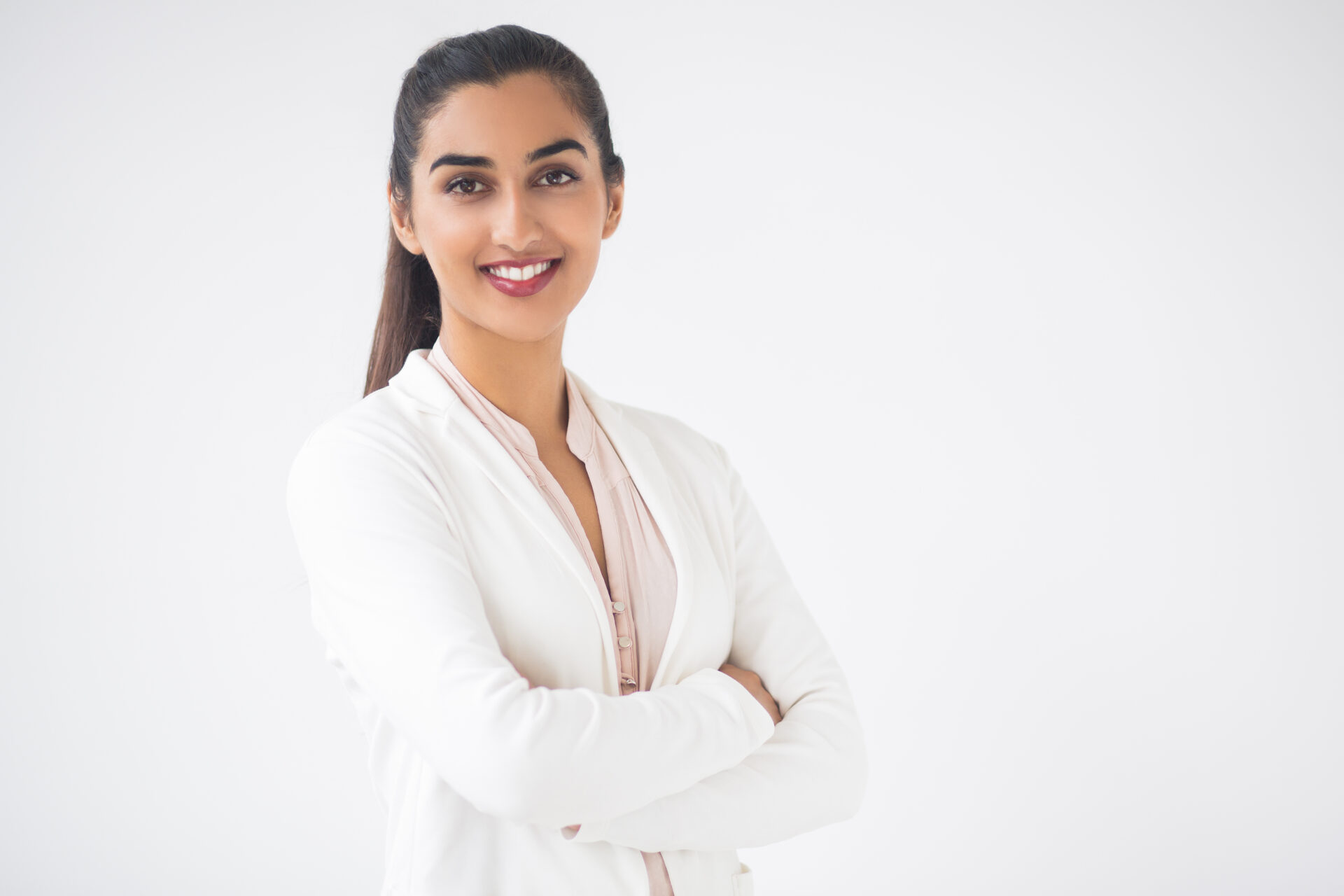 Closeup portrait of smiling young pretty Indian business woman looking at camera and standing with arms crossed. Isolated view on white background.