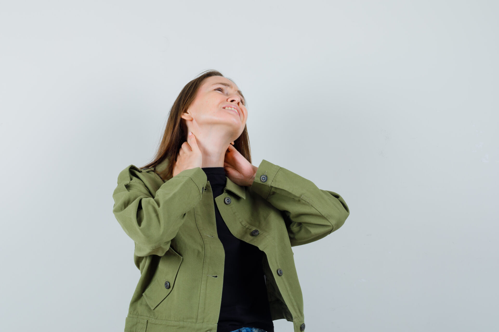 Young woman in green jacket suffering from neck pain and looking uncomfortable , front view.